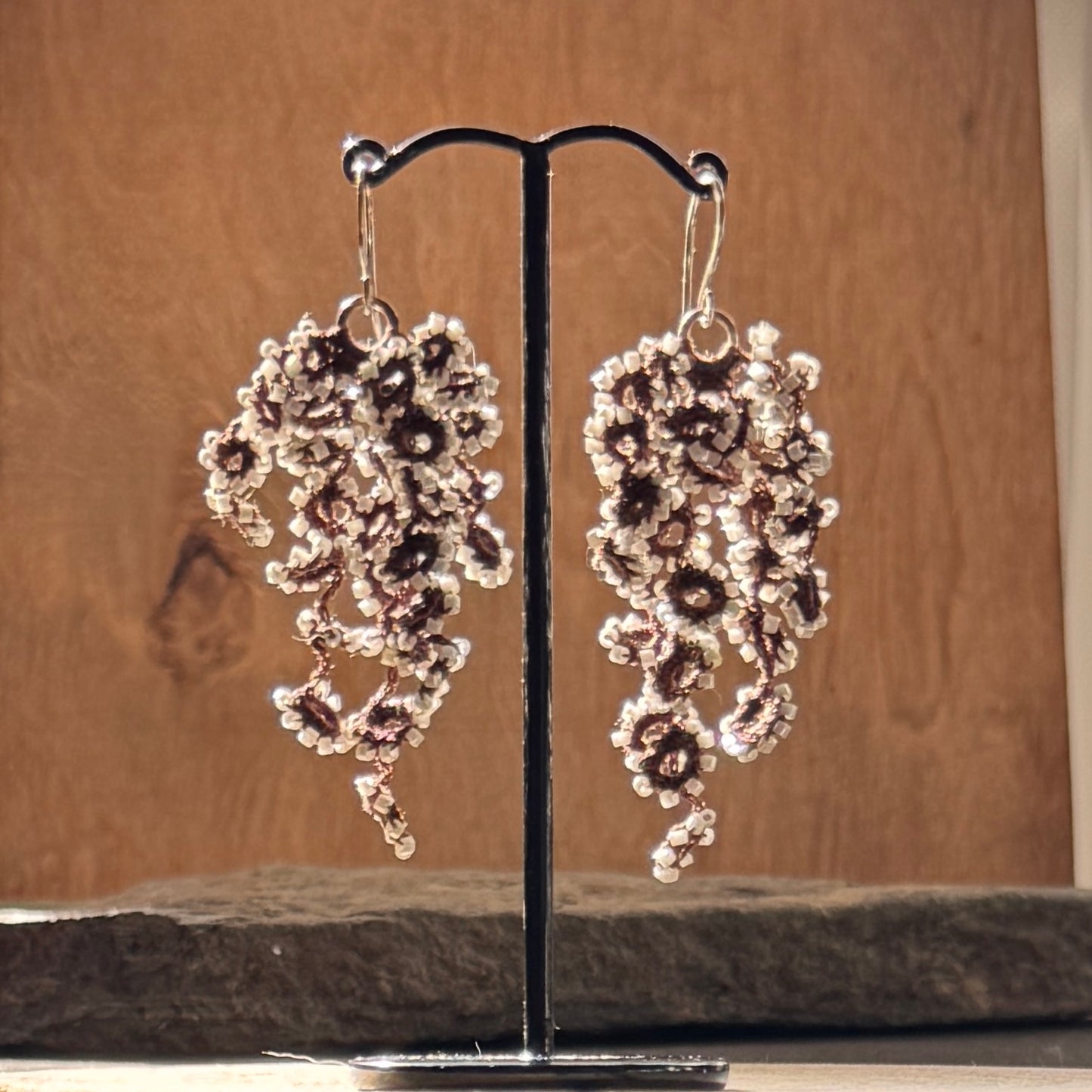 Pair of floral earrings on a stand against a wooden background