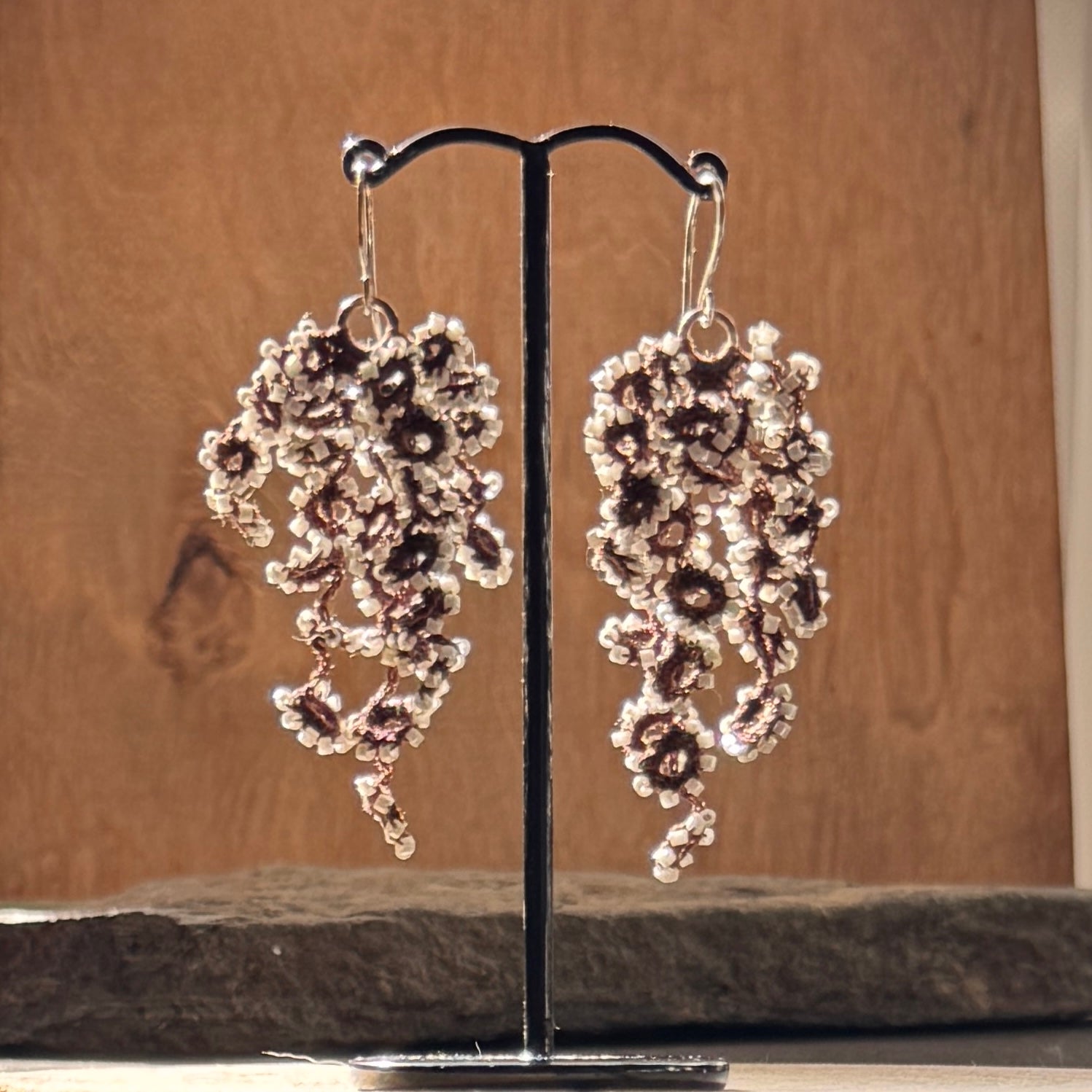 Pair of floral earrings on a stand against a wooden background