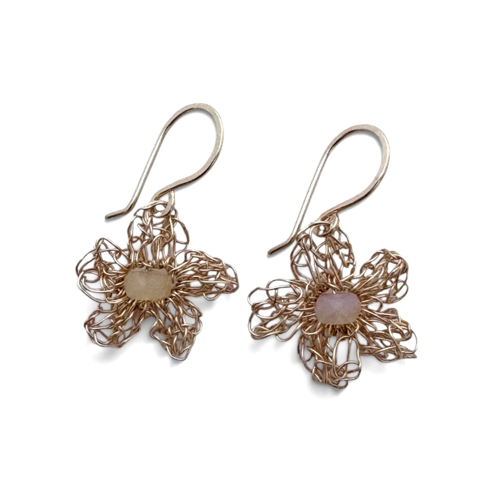 A pair of handmade flower-shaped drop earrings made from interwoven metallic wire in a warm gold tone, each featuring a smooth oval pale pink stone at the center, shown on a plain white background.