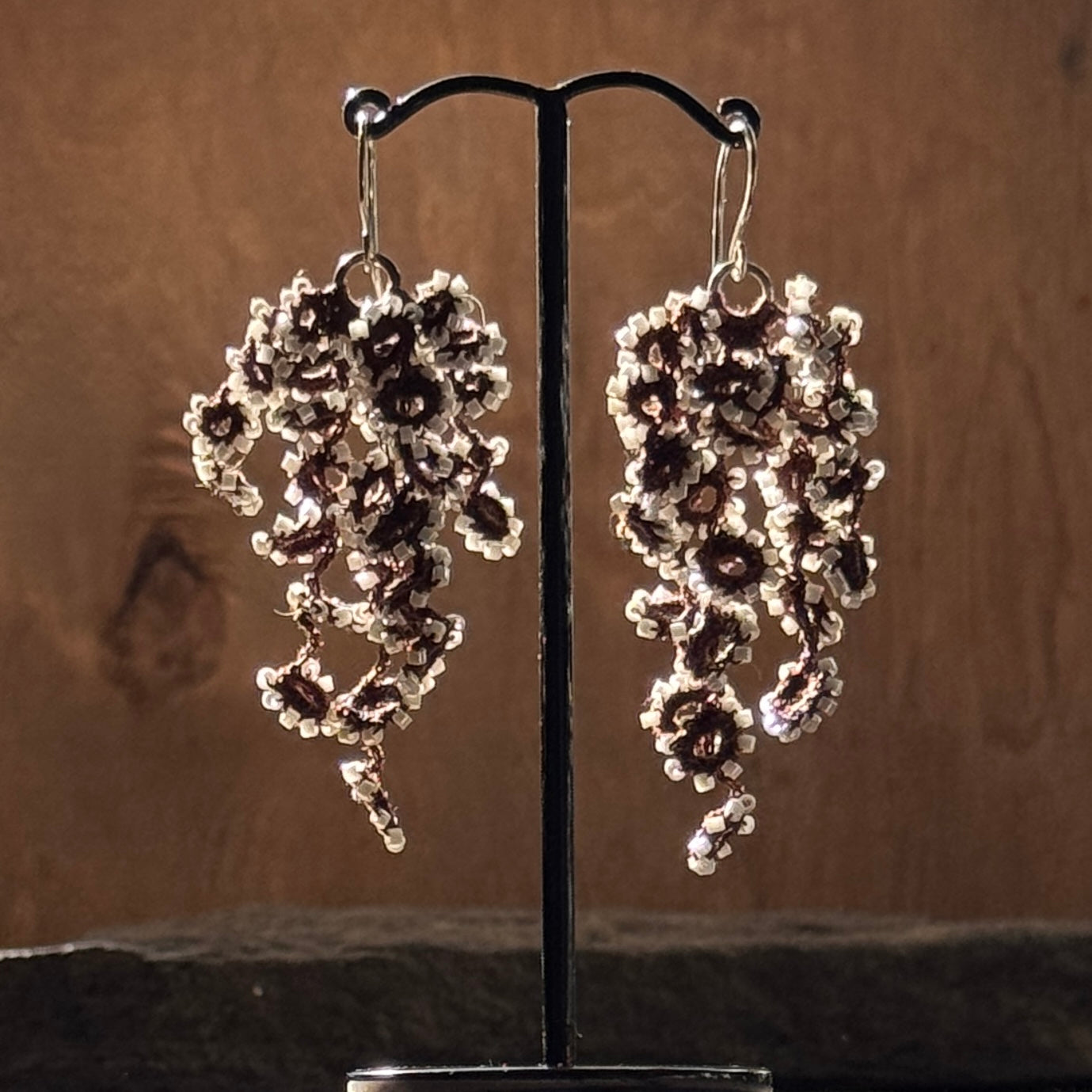 Pair of silver floral earrings on a stand against a brown background