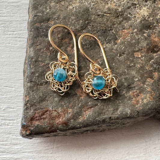 Gold earrings with blue gemstones on a stone surface