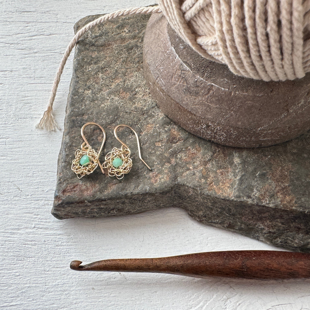 Gold earrings with turquoise stones on a stone surface next to a wooden crochet hook.