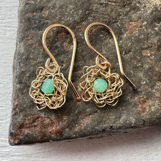 Gold wire-wrapped earrings with green stones on a stone surface