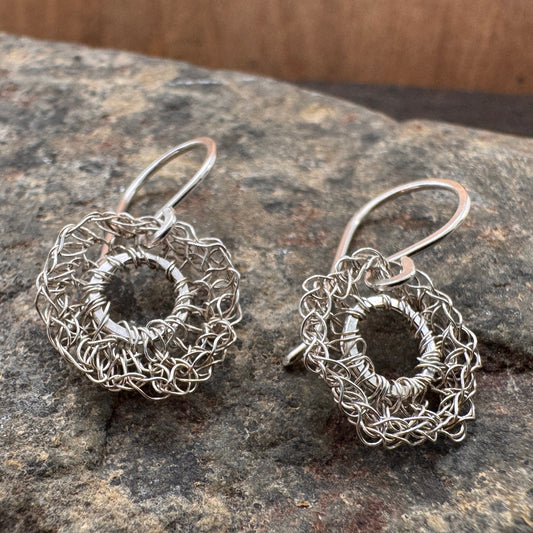 Silver wire-wrapped earrings on a stone surface