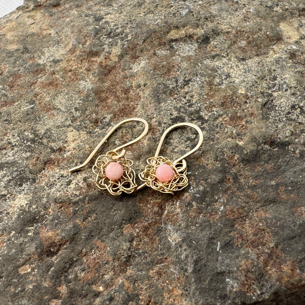 Gold earrings with pink stones on a textured stone surface