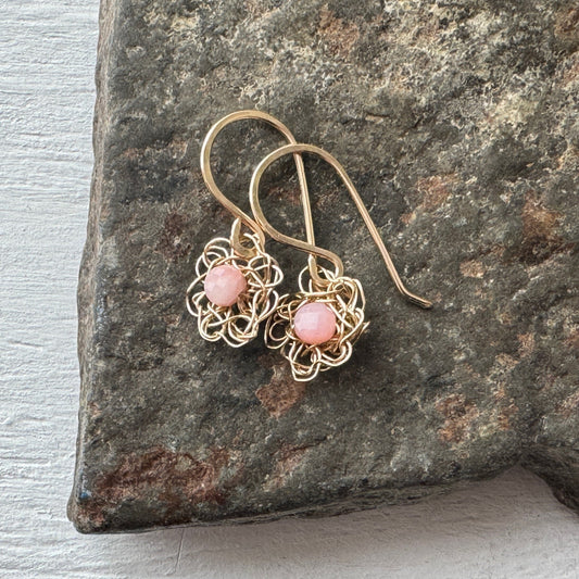 Gold earrings with pink stones on a stone surface